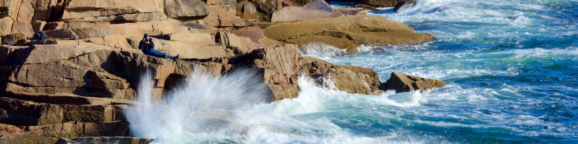 Costa rocosa con olas rompiendo contra las rocas y una persona tomando una fotografía.