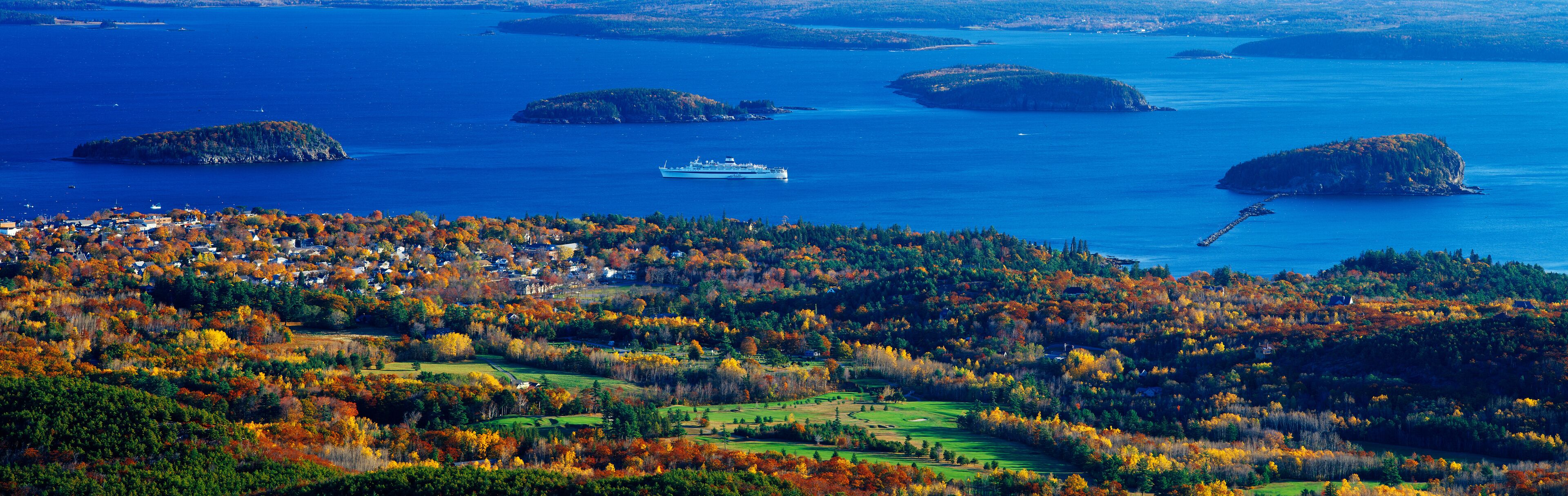 A coastal town with autumn foliage, a ferry, and several islands in the background.