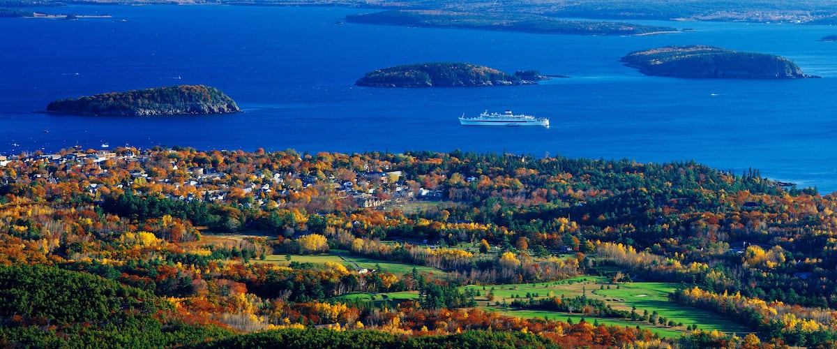 A coastal town with autumn foliage, a ferry, and several islands in the background.