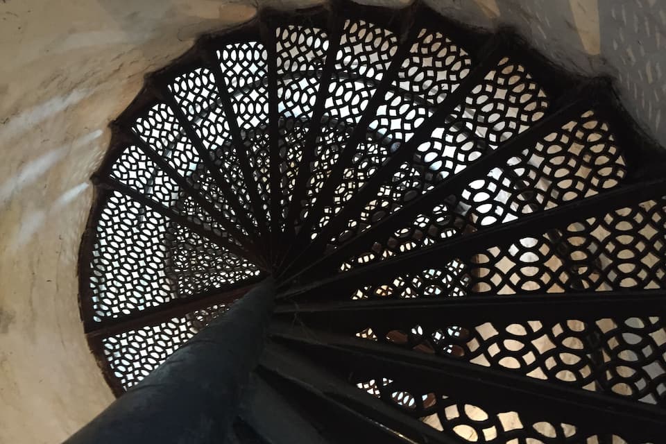 Un escalier en colimaçon doté d’une rampe métallique aux motifs géométriques.