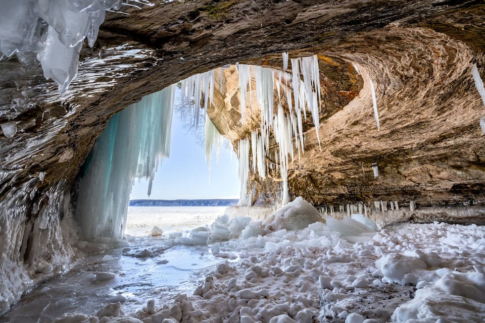 Una cueva de hielo con estalactitas colgando del techo y vistas a la playa.