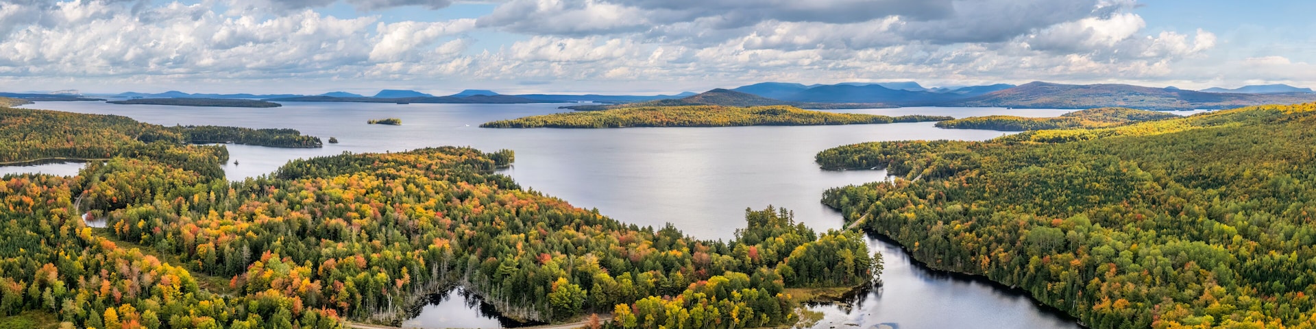 Un lac entourĂ© dâĂźles boisĂ©es, un ciel dĂ©gagĂ© et des montagnes Ă lâhorizon.