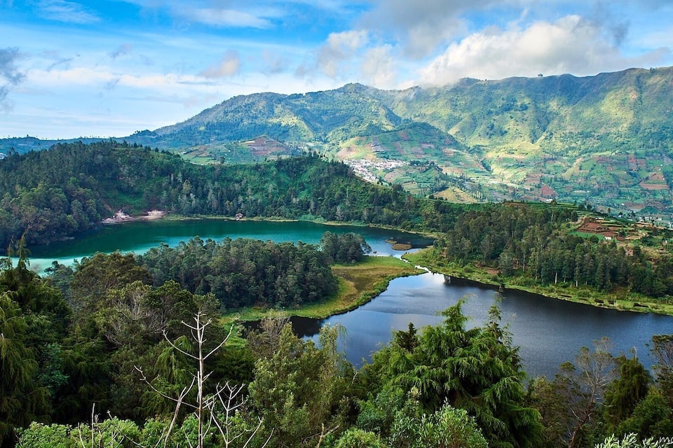 Un paisaje montañoso con un río y un lago pequeño rodeado de bosque denso.
