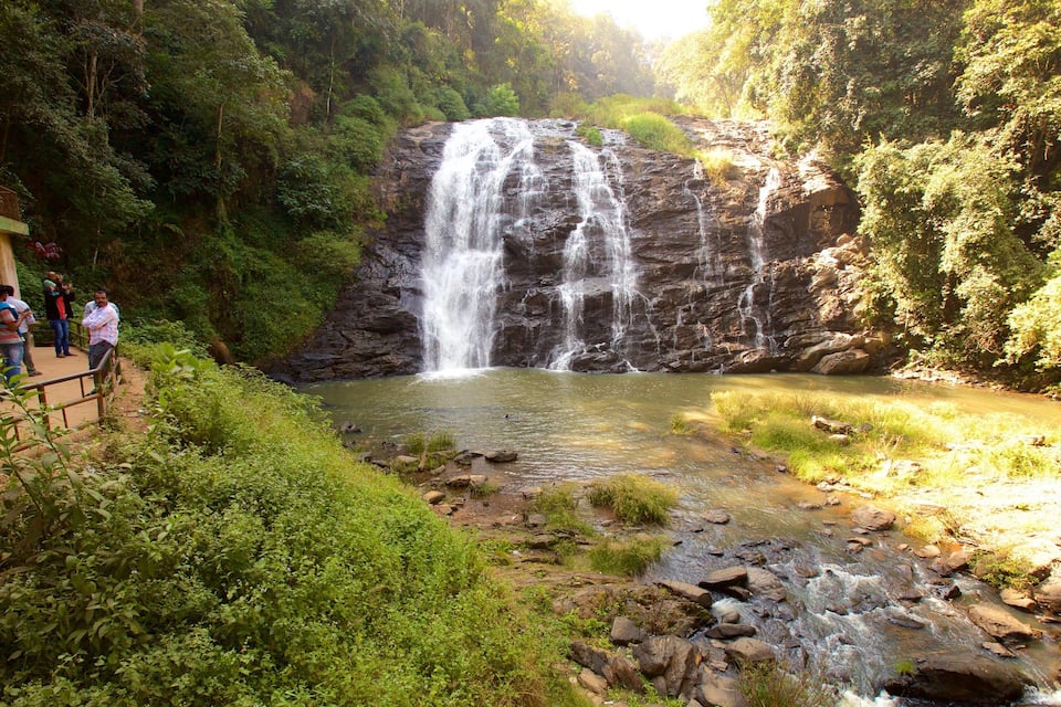 A waterfall cascading over rocks into a river surrounded by lush greenery.