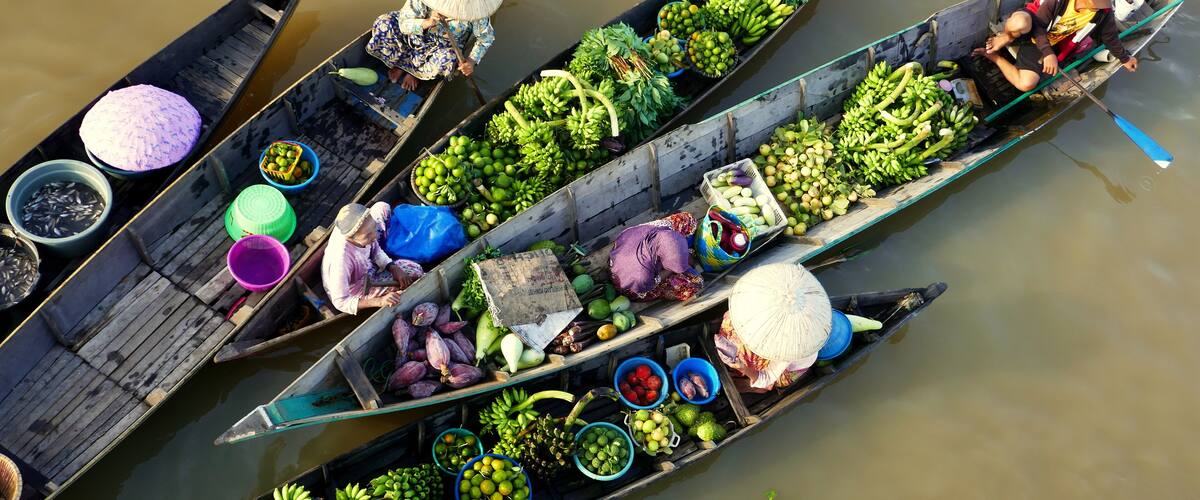 A group of canoes loaded with various fruits and vegetables on a calm river.