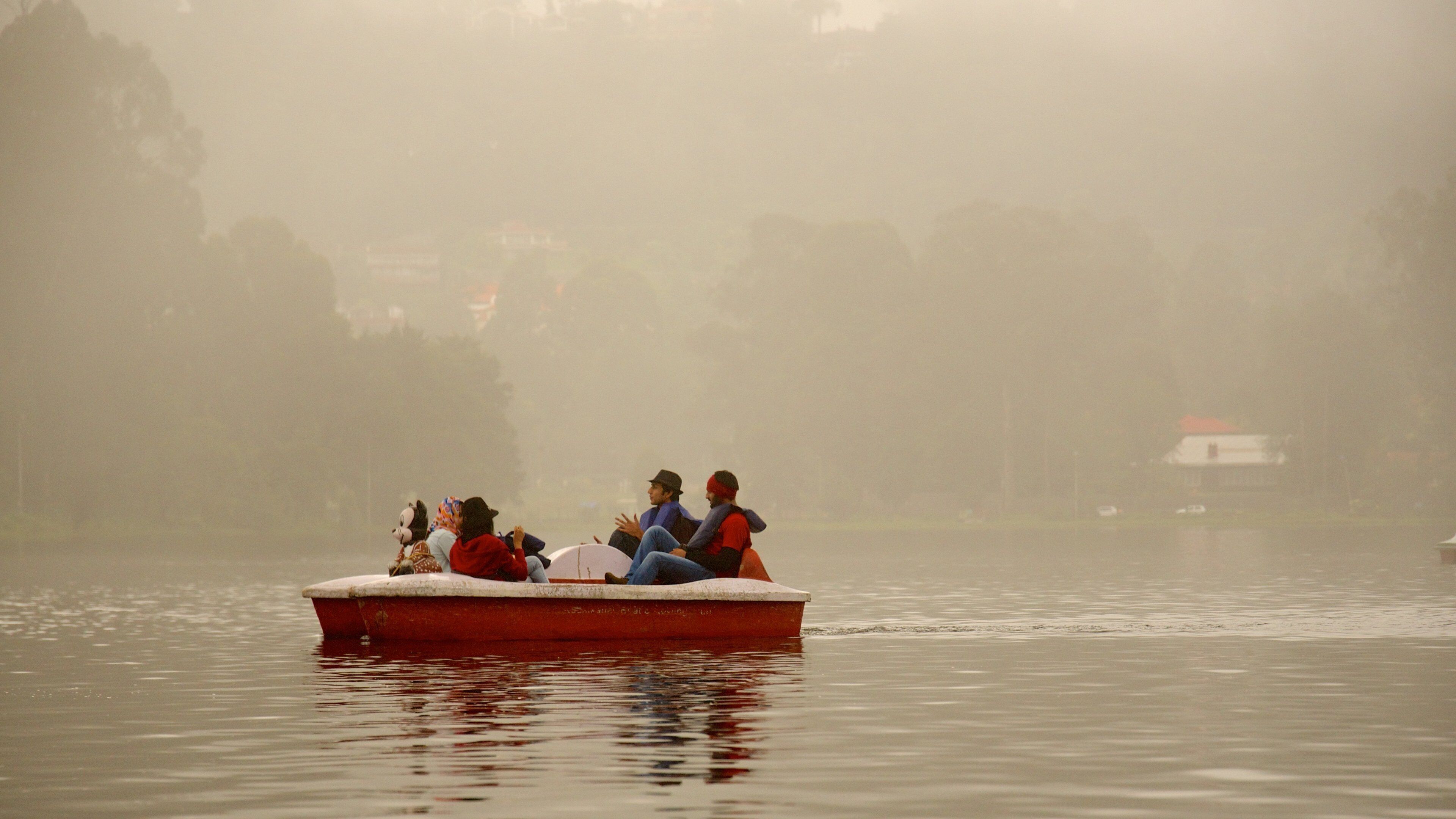 A foggy lake with a red boat carrying people.