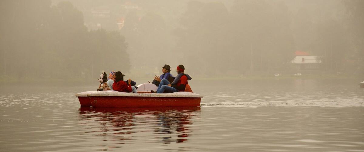 A foggy lake with a red boat carrying people.