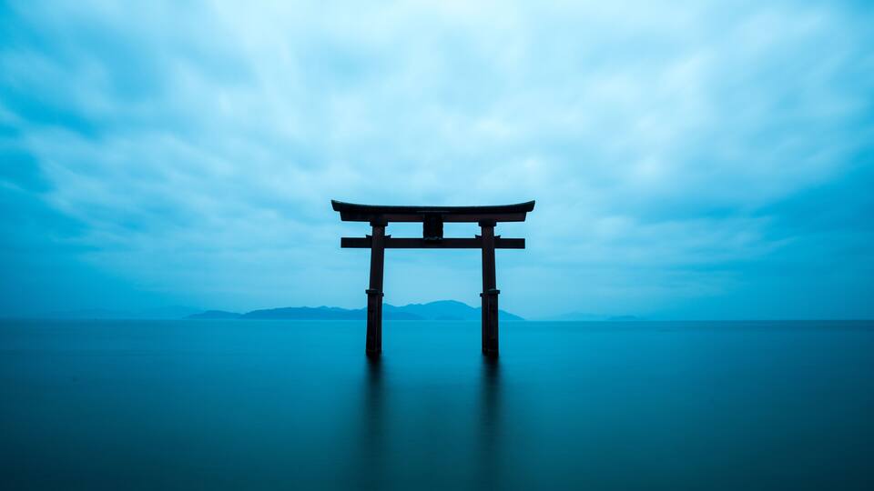 A torii gate in the water with mountains in the background.
