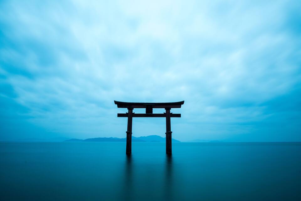 Un torii a l'aigua amb muntanyes al fons.