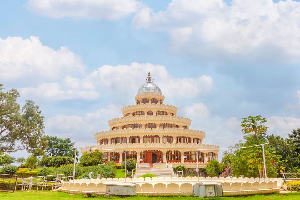 A large, ornate building with a central dome and multiple tiers, surrounded by lush greenery and a well-maintained garden.