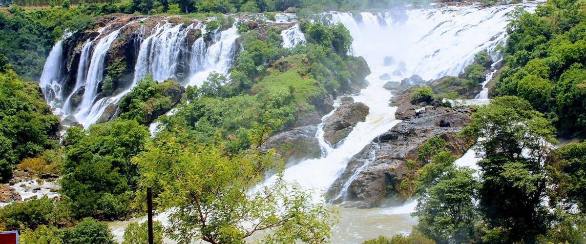 A multi-tiered waterfall surrounded by lush greenery and mountains in the background.