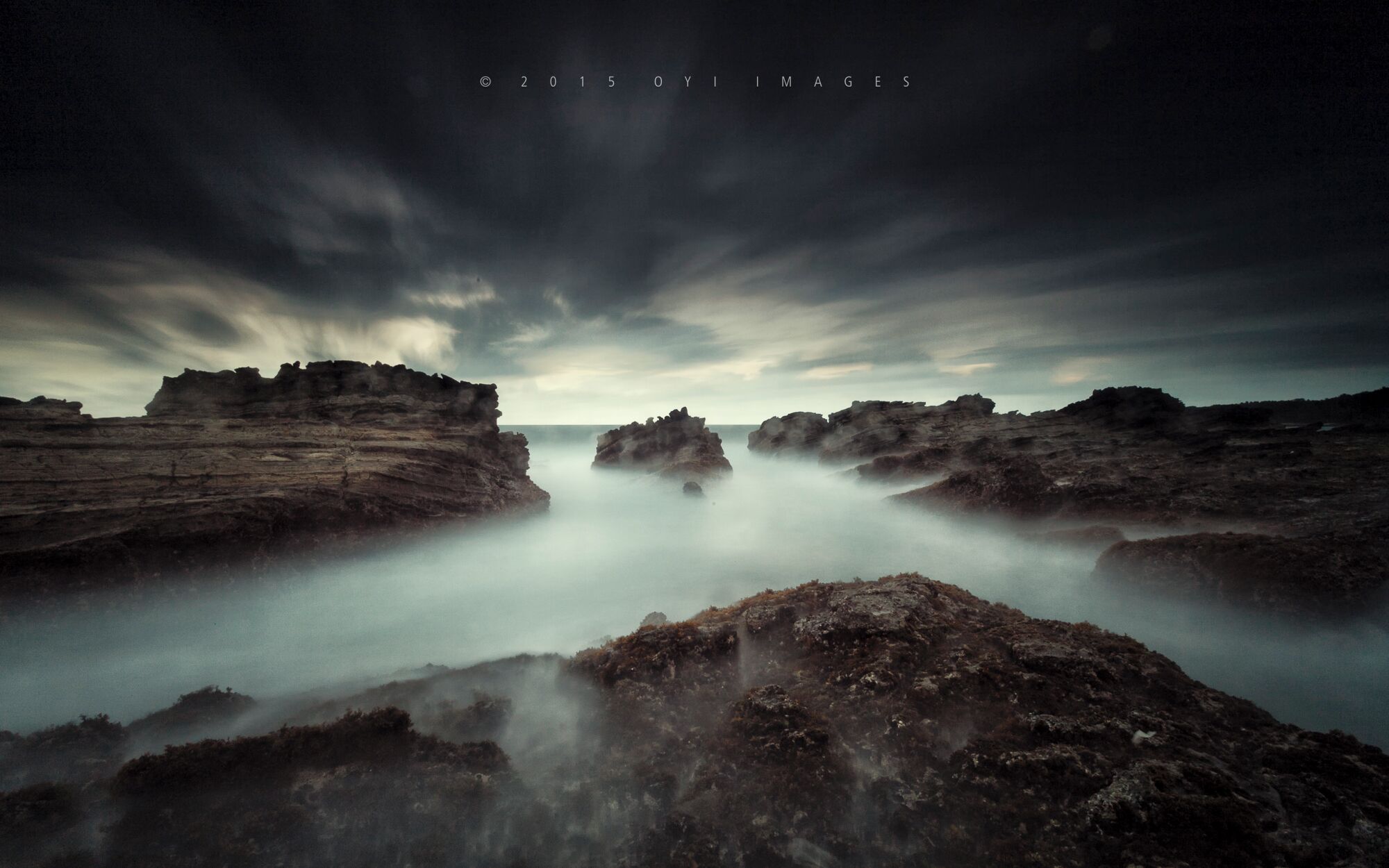 A coastal landscape with rocky formations and a misty atmosphere.