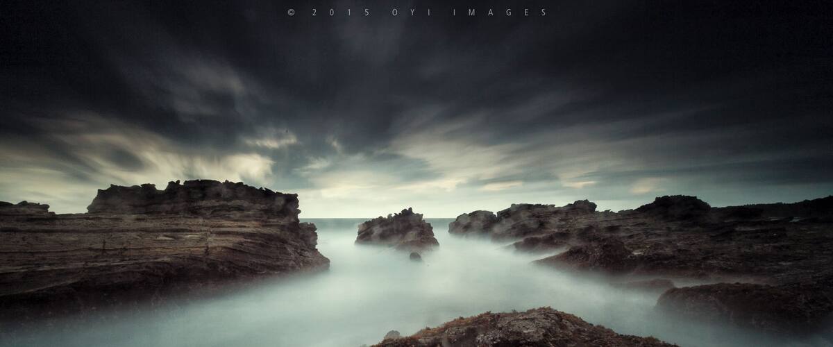 A coastal landscape with rocky formations and a misty atmosphere.