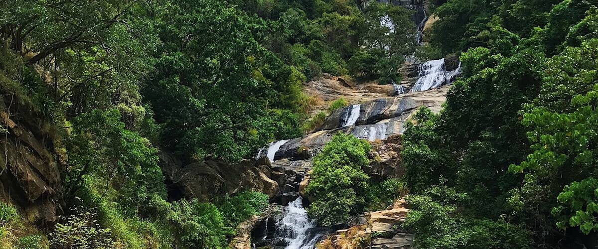 A multi-tiered waterfall cascading down a rocky hillside surrounded by lush greenery.