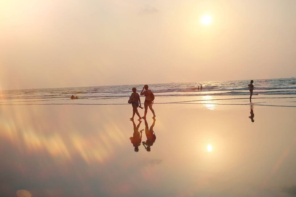 A beach at sunset with people walking and reflecting on the wet sand.