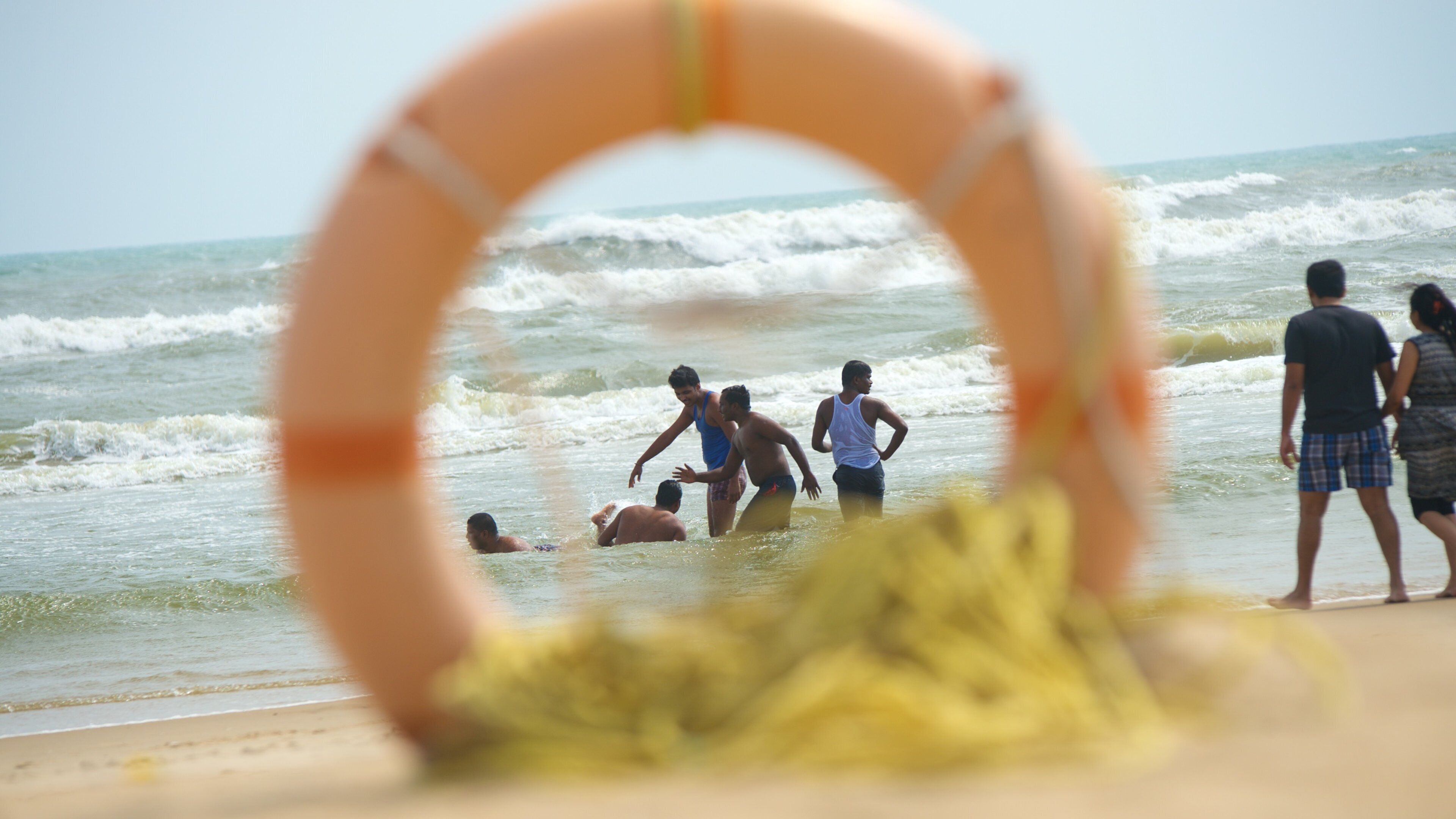 A lifeguard ring on a beach with people in the water and on the shore.