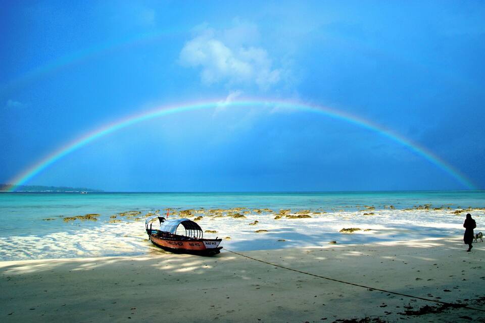 Een boot op een zanderig strand met een regenboog aan de lucht.