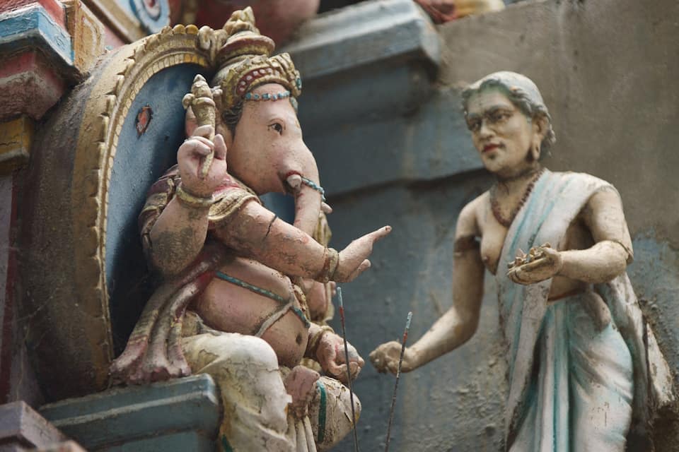 A weathered statue of a deity with a child, set against a stone structure.