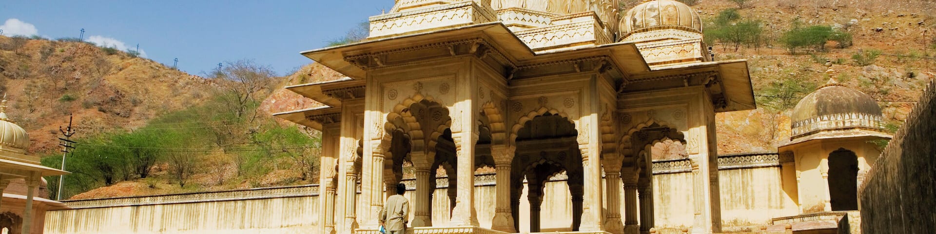 A historic building with domes and arches, set against a hilly backdrop.