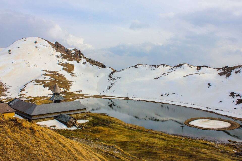 A snow-covered mountain landscape with a small building and a pond.