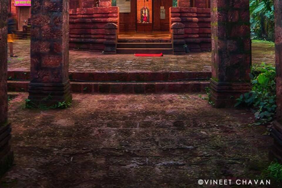 Un temple orné d’une inscription dans une langue locale, entouré de piliers de pierre et surplombé d’un ciel nuageux.