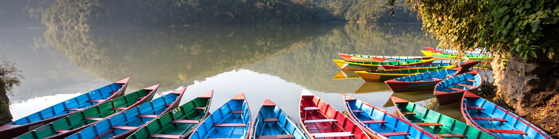 Una hilera de botes coloridos amarrados a un muelle a orillas de un lago, con montañas al fondo.