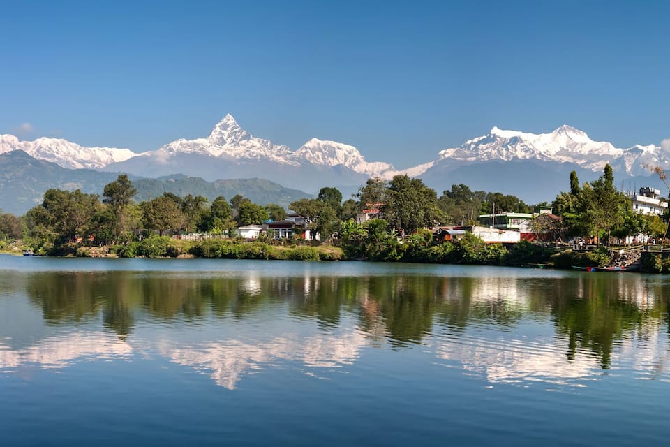 Un lac paisible où se reflètent les montagnes, une petite ville avec ses maisons et une végétation luxuriante.