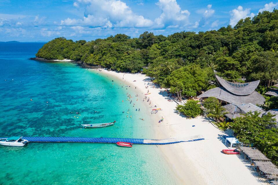 Een tropisch strand met helder turquoise water, een wit zandstrand en weelderige groene begroeiing.