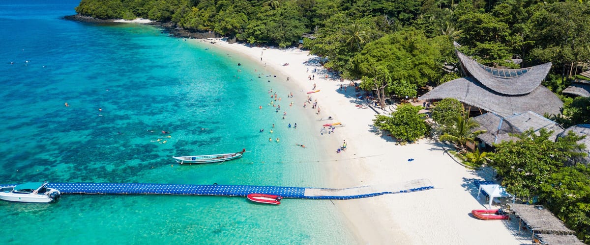 A tropical beach with clear turquoise waters, a white sandy shore, and lush green vegetation.