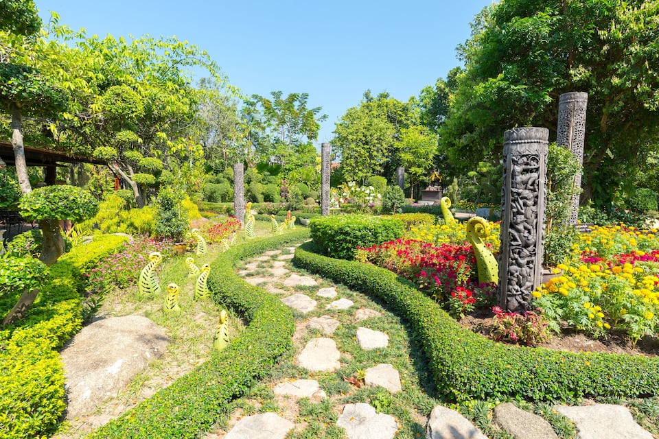 A garden with a stone path, lush greenery, and decorative statues.