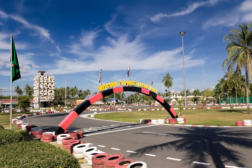 Ingang van een racecircuit met een bord waarop staat 'WELCOME TO RACING LANE' en een opvallend gebouw op de achtergrond.
