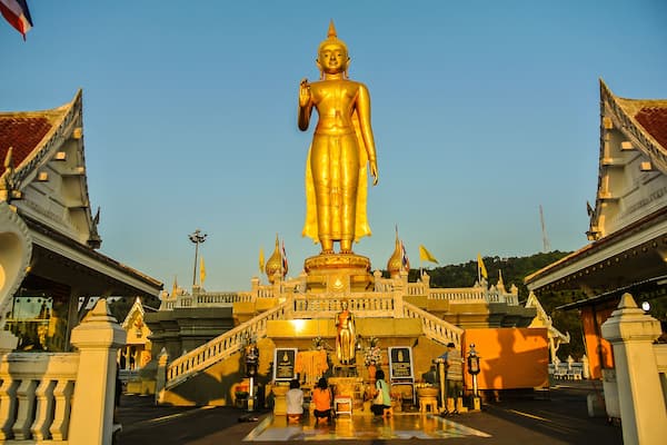 A large golden Buddha statue at the entrance of a temple complex with traditional architecture.