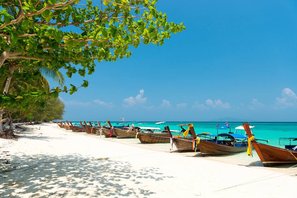 A beach with rows of wooden boats and a clear blue sky.