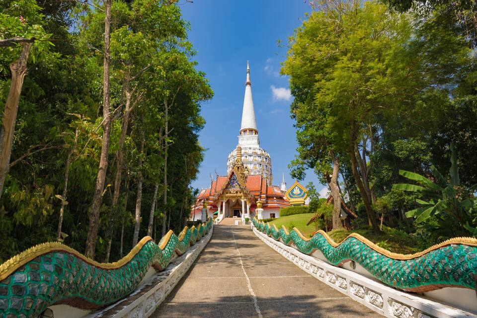 A temple with a spire, surrounded by trees and a pathway with decorative railings.