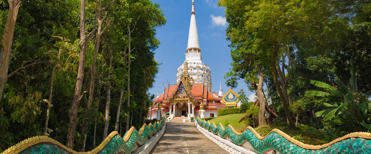 A temple with a spire, surrounded by trees and a pathway with decorative railings.