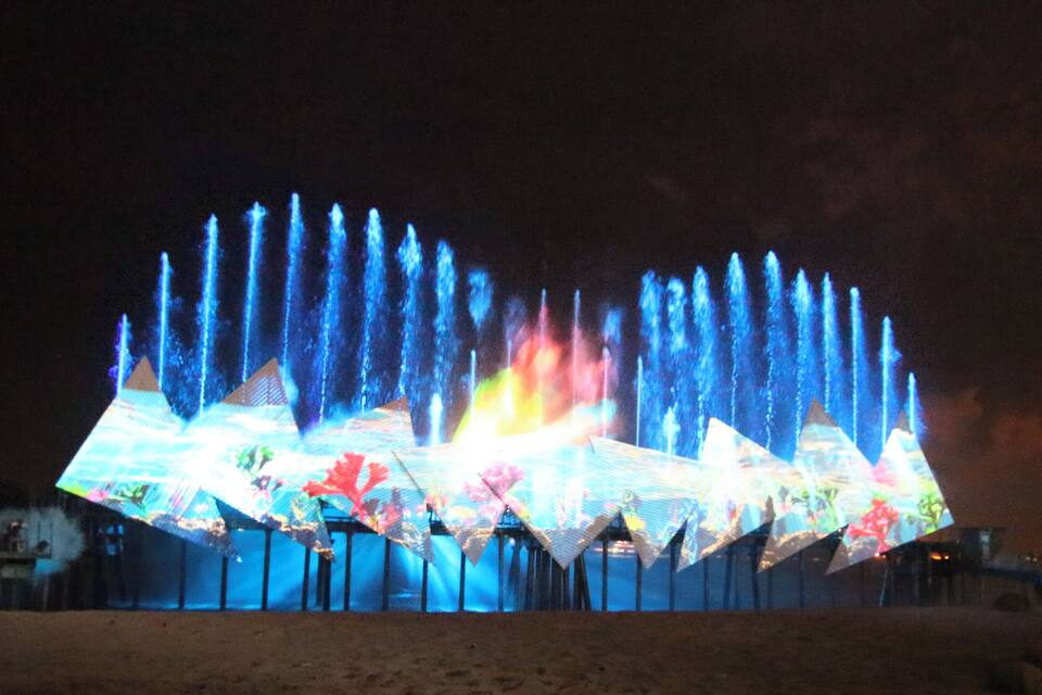 A nighttime water fountain display with illuminated geometric shapes and water jets.