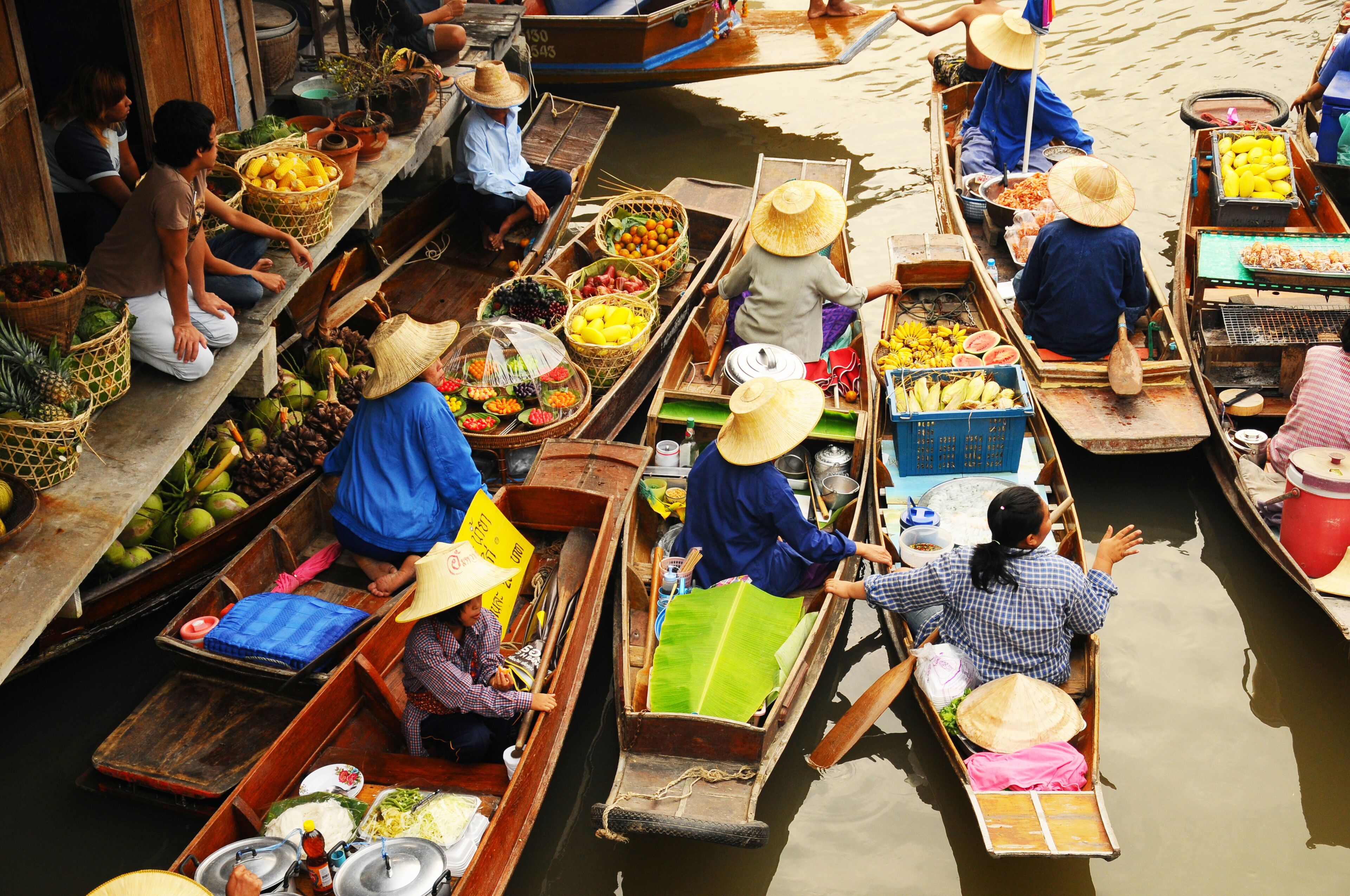 A group of canoes on a river, each carrying various fruits and vegetables.