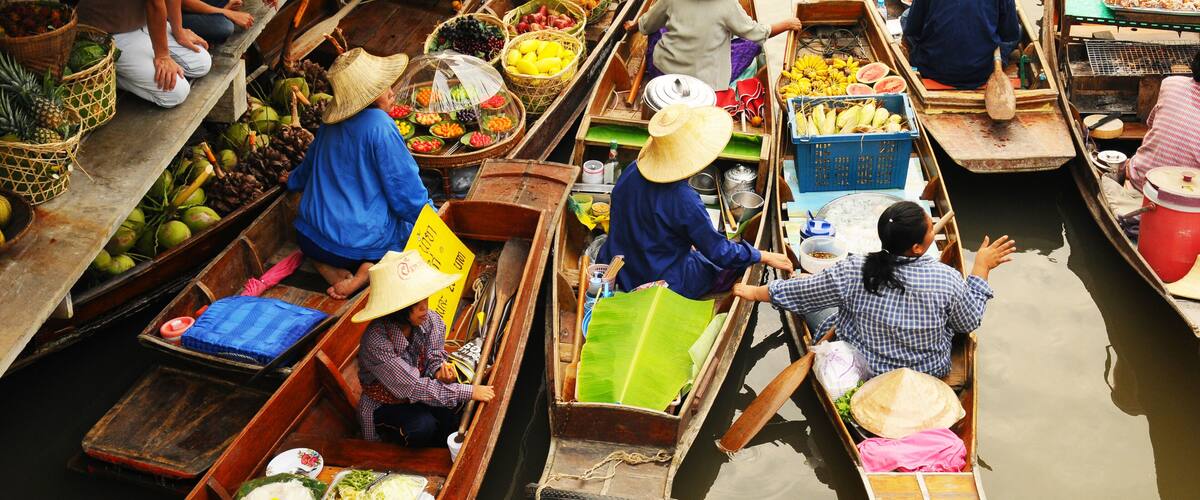 A group of canoes on a river, each carrying various fruits and vegetables.
