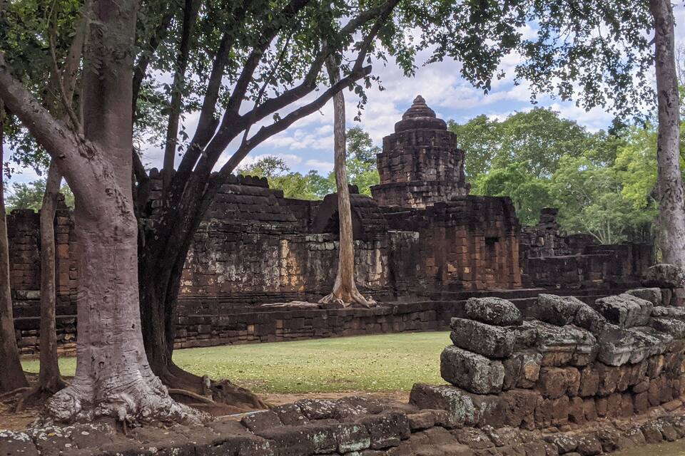 An ancient temple with large trees in the foreground and a clear sky in the background.
