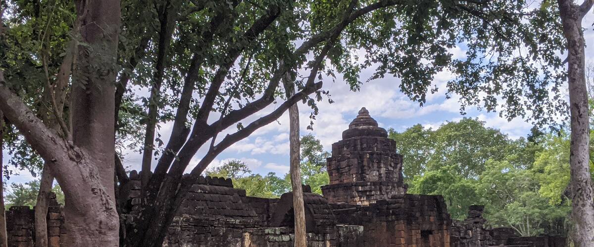 An ancient temple with large trees in the foreground and a clear sky in the background.