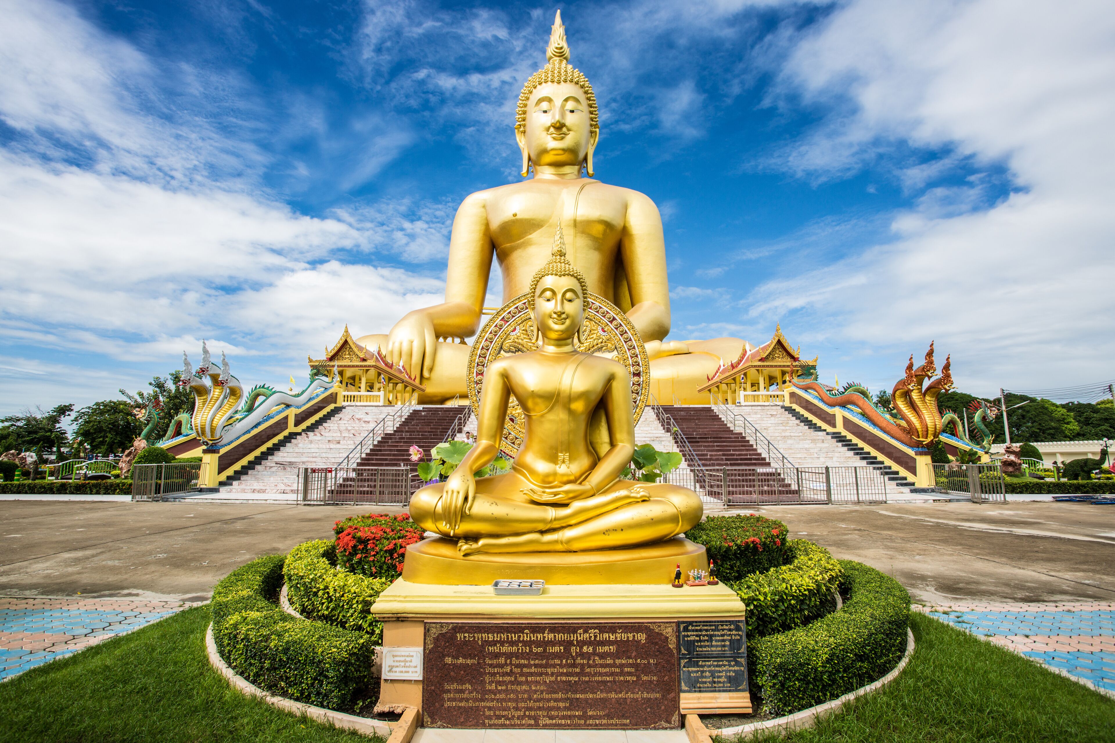 A large golden Buddha statue with a smaller figure in front, surrounded by a temple complex with stairs and traditional architecture.