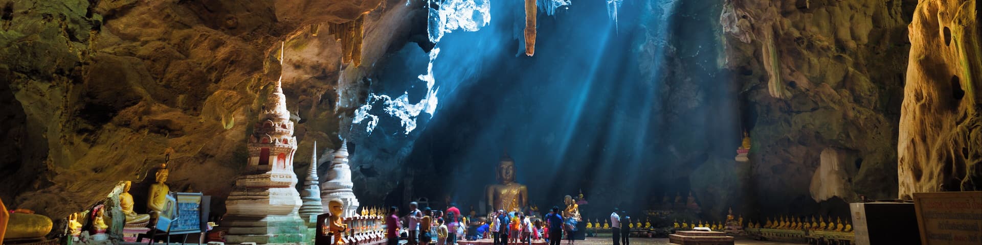 Un temple troglodyte orné de stalactites, une statue de Bouddha et des visiteurs.