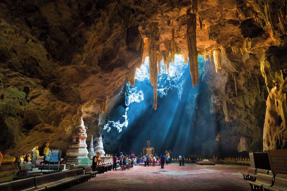 Un temple troglodyte orné de stalactites, une statue de Bouddha et des visiteurs.