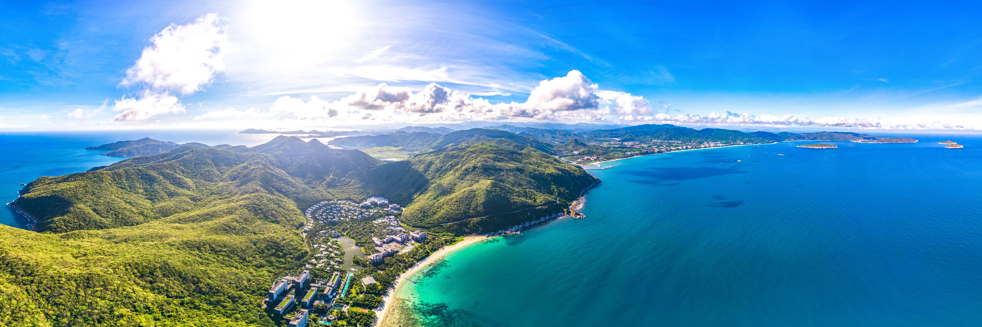 A coastal landscape with lush green hills, a beach, and clear blue waters.