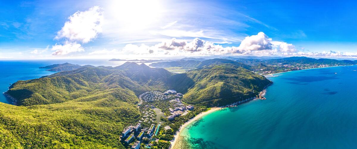 A coastal landscape with lush green hills, a beach, and clear blue waters.