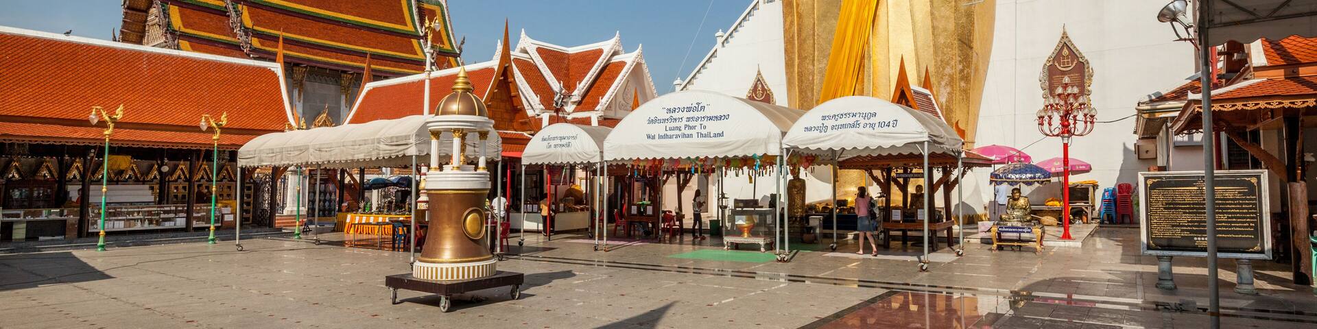 A large golden Buddha statue in front of traditional Thai architecture.