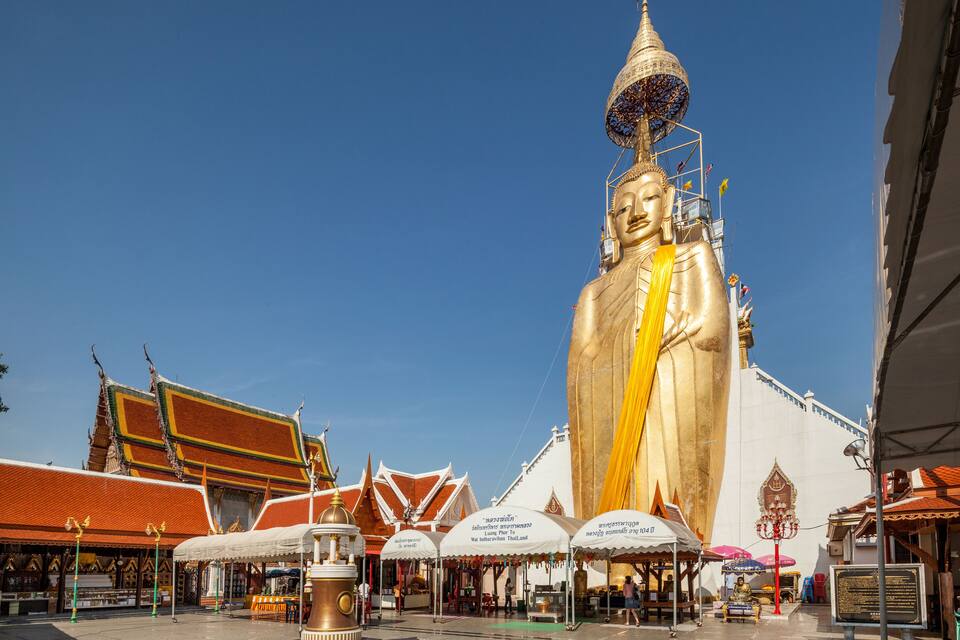 A large golden Buddha statue in front of traditional Thai architecture.