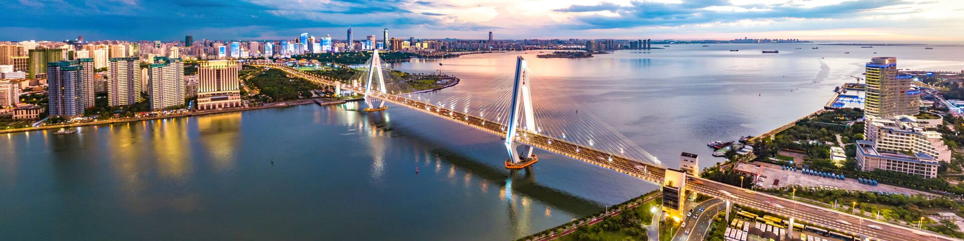 A modern cityscape with a prominent cable-stayed bridge over a river, surrounded by high-rise buildings and a clear sky.