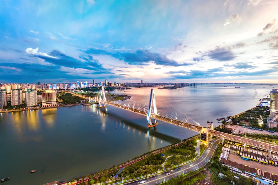 A modern cityscape with a prominent cable-stayed bridge over a river, surrounded by high-rise buildings and a clear sky.