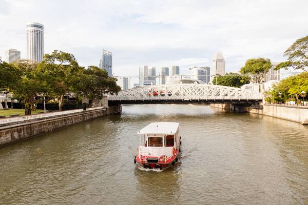 KBB7M1 A boat ply the Singapore River on Boat Quay toward Anderson Bridge, with the city's skyline in the background.